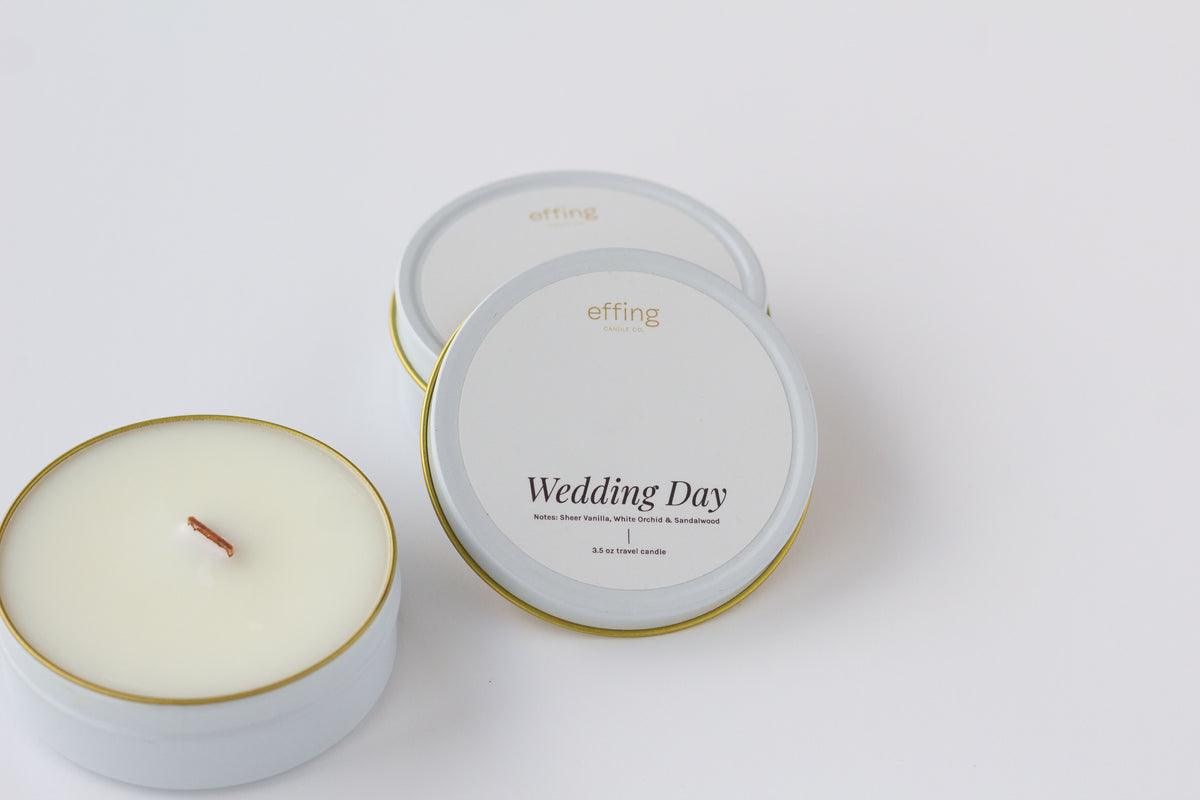 Two round tin candles on a clean white background, including one open candle showing the wax and wood wick, and one closed lids with the label 'Wedding Day' and brand 'effing candle co'.