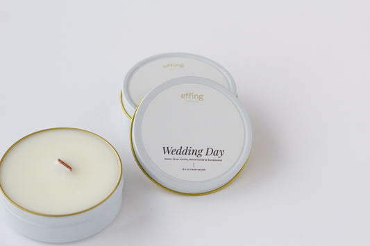 Two round tin candles on a clean white background, including one open candle showing the wax and wood wick, and one closed lids with the label 'Wedding Day' and brand 'effing candle co'.
