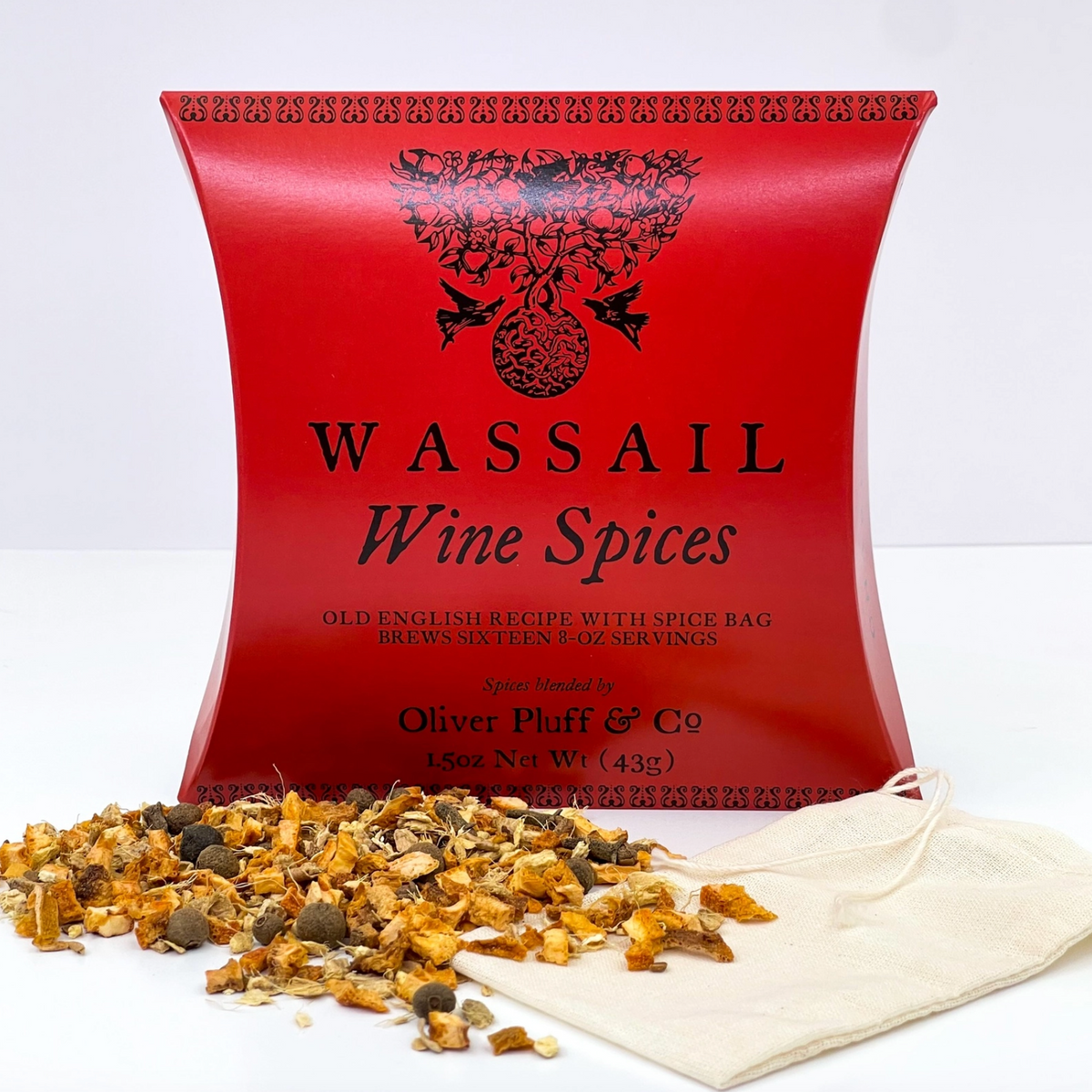 A red Wassail Wine Spices box with black lettering, shown on a white background with loose dried spices spilled in front and a small beige drawstring bag beside it. Visible brand text includes Oliver Pluff & Co.