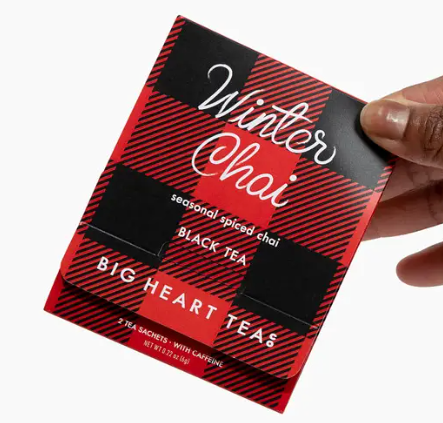 A two-tea sachet package of Winter Chai tea in a red and black winter plaid pattern, with a hand holding the package against a white background. 