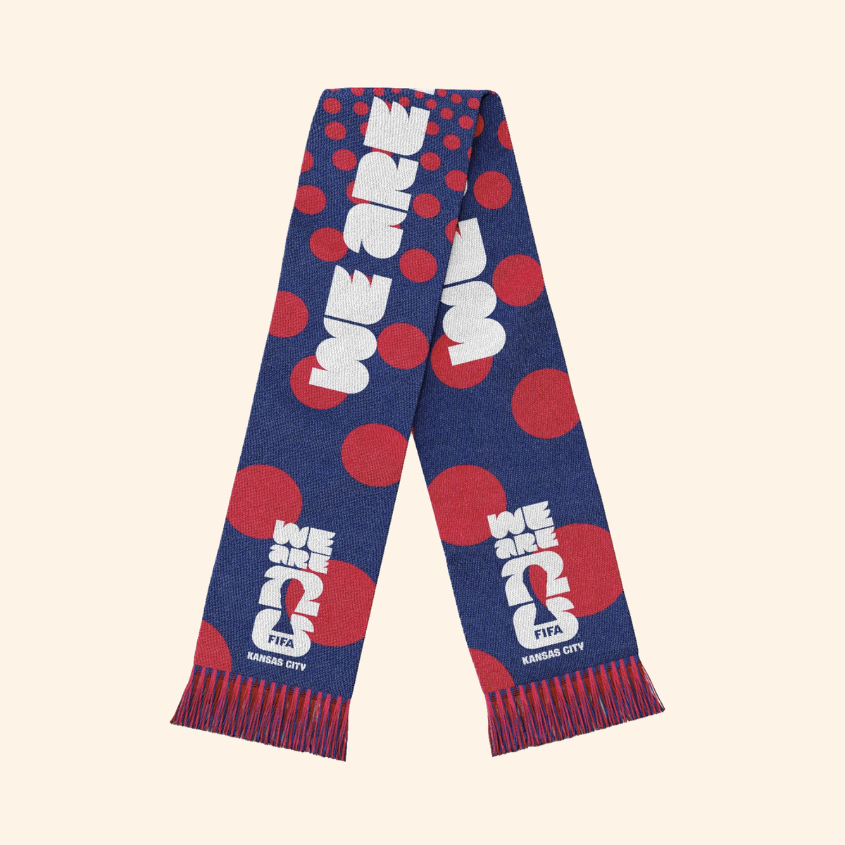 A navy blue knit scarf with red polka dots and white text reading 'WE ARE 2025 FIFA KANSAS CITY', laid flat on a light beige background.