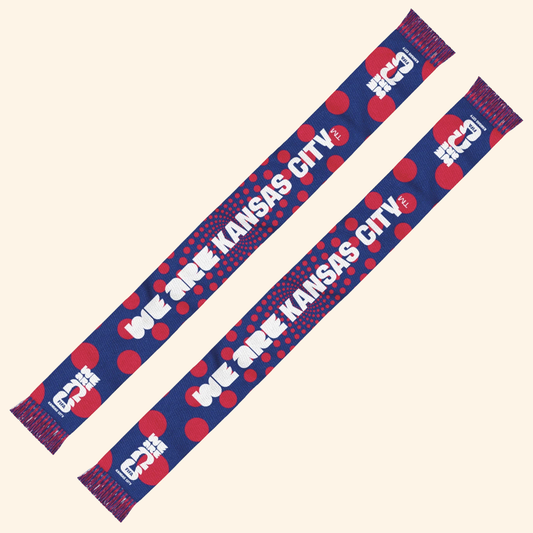 Two matching blue and red knit scarves with white text reading 'WE ARE KANSAS CITY 2026' printed repeatedly, shown on a plain light beige background.