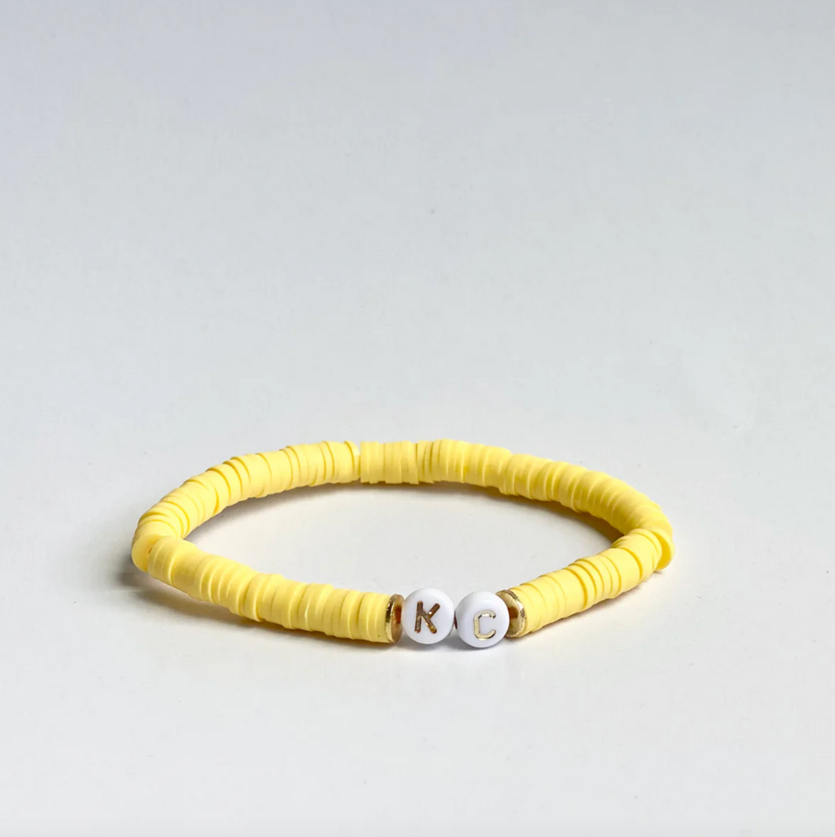 Yellow beaded friendship bracelet with white and gold letter beads spelling out "KC"
