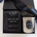 Load image into Gallery viewer, A gift set featuring a black box with a black satin ribbon, containing a black coffee bag labeled 'START Coffee Co. Signature Blend' and a silver glass jar candle with a silver lid and a circular black-and-white label reading 'Smoke Signals'.
