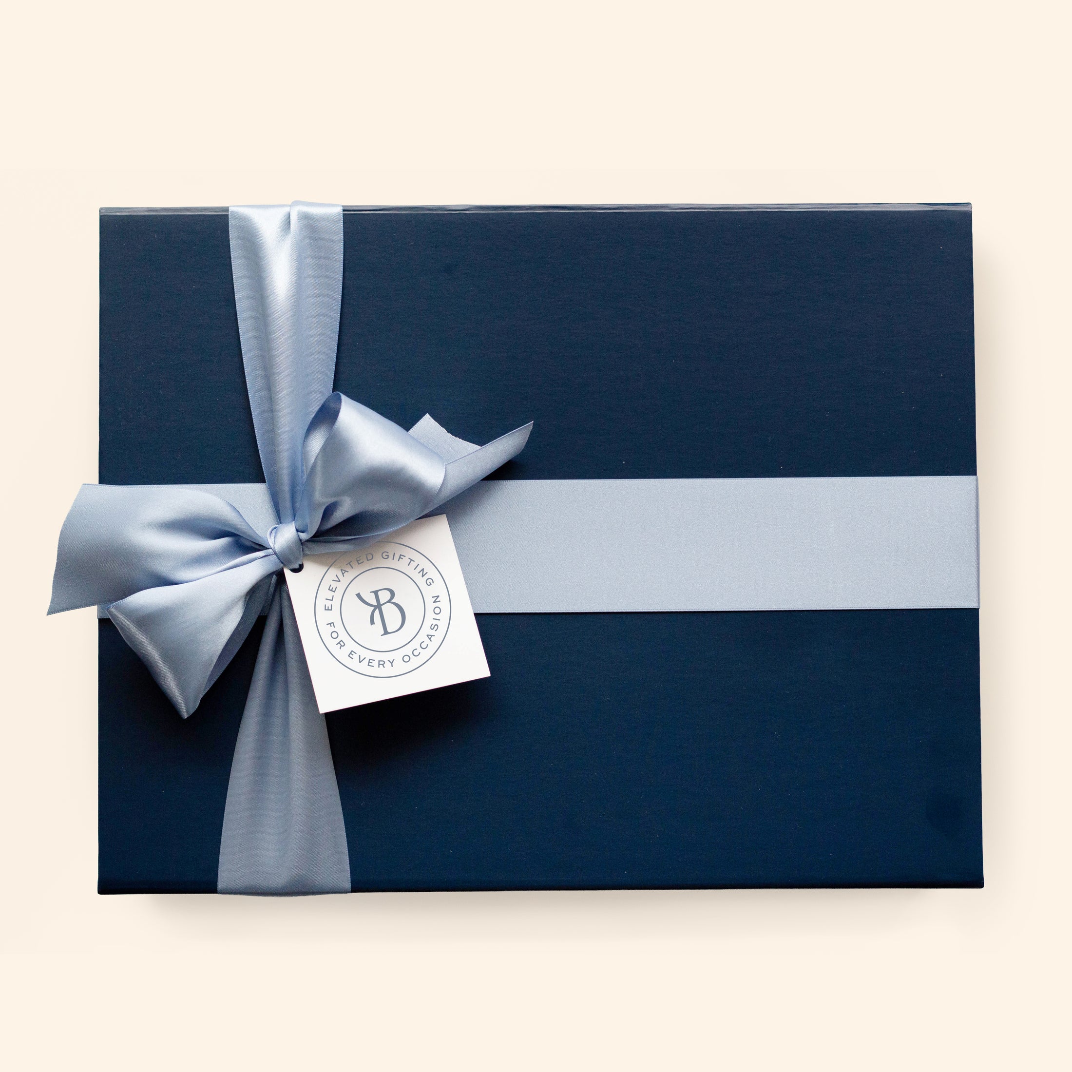 A navy blue high quality cardboard gift box wrapped with a light blue satin ribbon and bow, featuring a white tag with a circular logo.